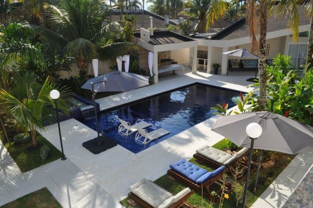 Piscina da Pousada Village Cozumel com um espaço amplo ao redor da piscina com árvores e sofás para se sentar