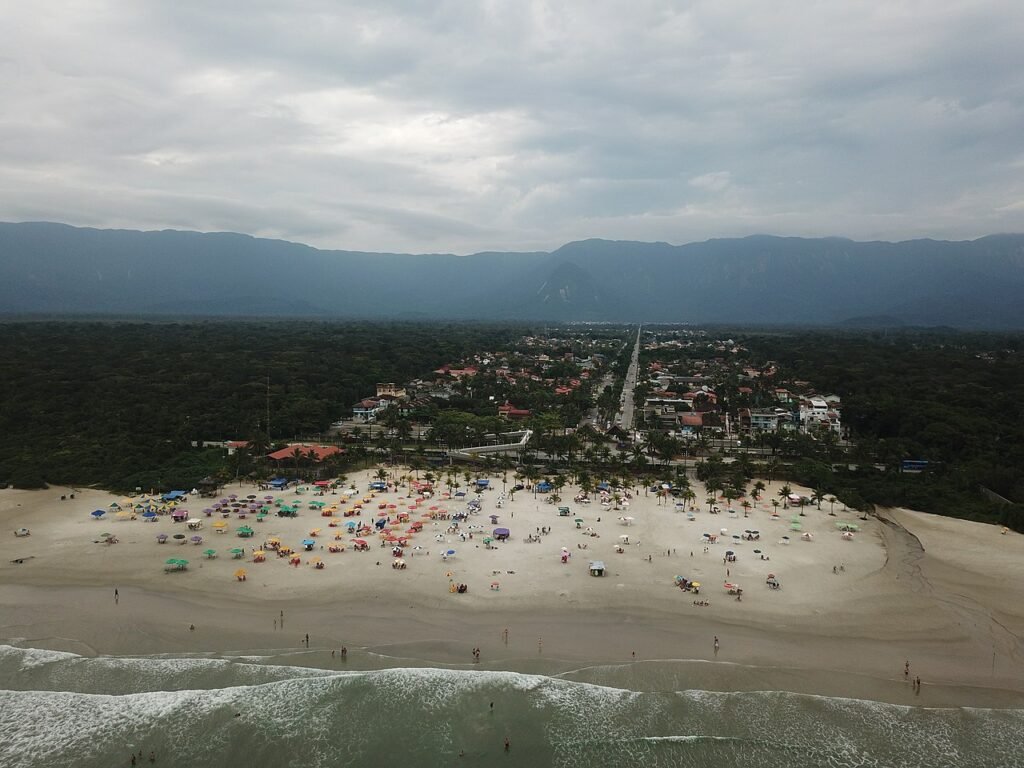Praia de Boracéia. Vista do mar de frente para a cidade, muitas pessoas na areia e atrás árvores e a cidade.