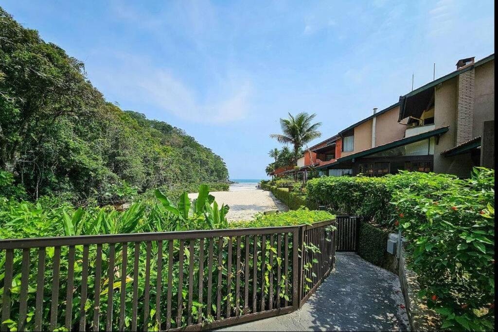 Vista da Casa em Condomínio Pé na Areia na Praia do Engenho durante o dia com jardim a frente e ao fundo a praia.