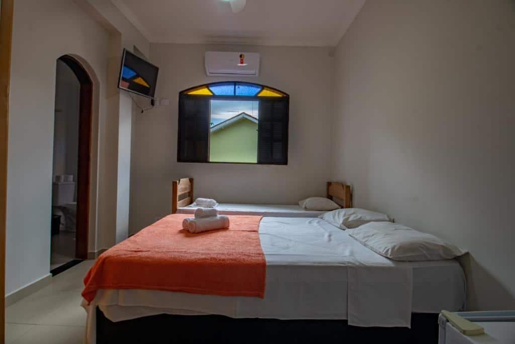 Quarto da Pousada do Vladimir. Uma cama de casal e uma cama de solteiro no lado direito. Do lado da cama de solteiro uma janela. De frente para as camas a porta do banheiro e uma televisão. Foto para ilustrar post sobre Pousadas em Boracéia.