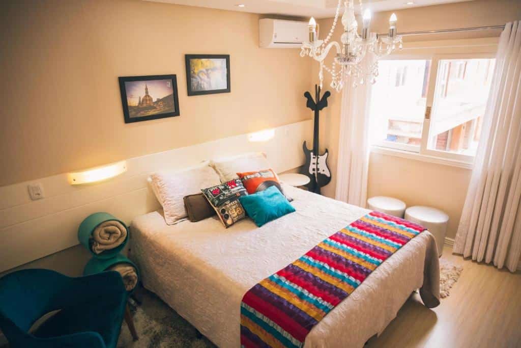 Quarto no Ap de Cinema! No centro!, local igualmente decorado em estilo vintage, uma cama de casal com muitas almofadas coloridas, dois quadrinhos, um ar-condicionado, uma janela com cortina e dois bufes, para representar airbnb em Gramado