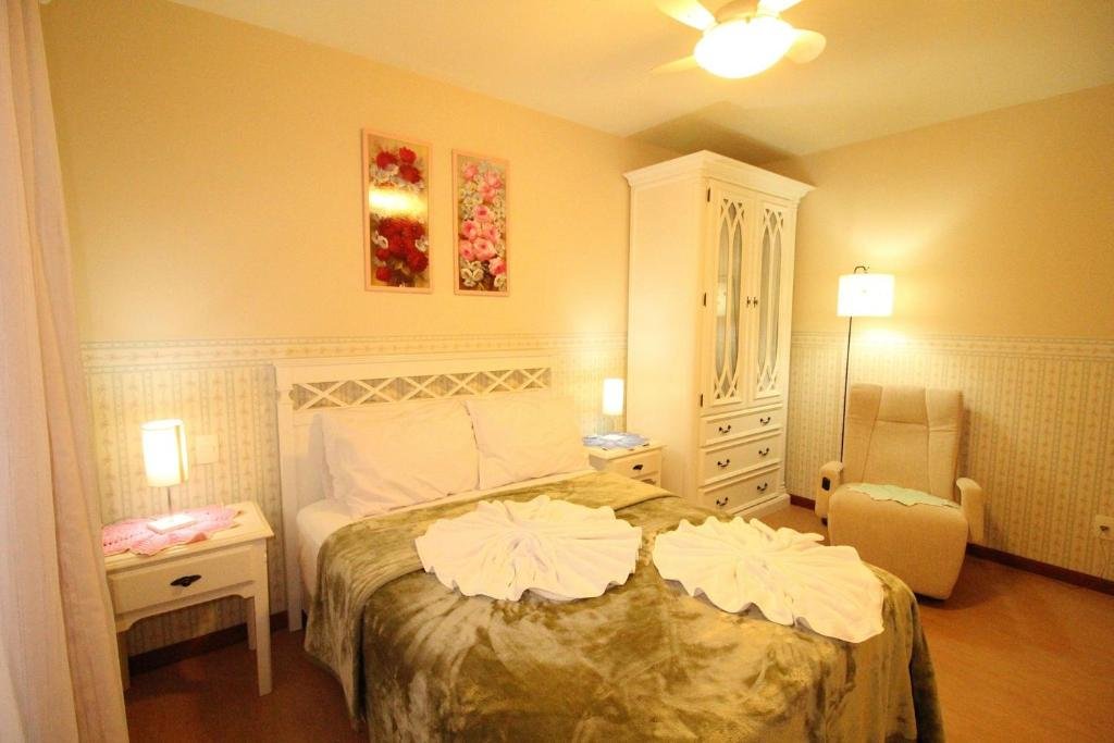 Quarto no Araucárias 302, uma cama de casal, uma poltrona, um abajur, um armário, dois quadros e uma janela, para representar airbnb em Gramado