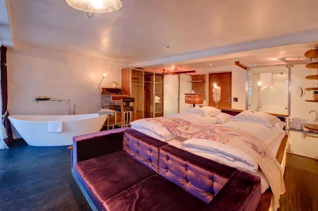 Quarto do Backstage Boutique SPA Hotel com cama de casal do lado direito da imagem, no pé da cama uma sofá de dois lugares e do lado direito do ambiente uma banheira de hidromassagem. Representa onde ficar em Zermatt.