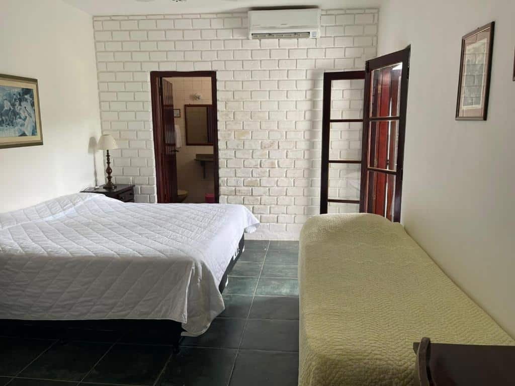 Quarto da Barequeçaba Praia Hotel com cama de casal, cômoda de madeira do lado esquerdo com luminária e cama de solteiro do lado direito.
