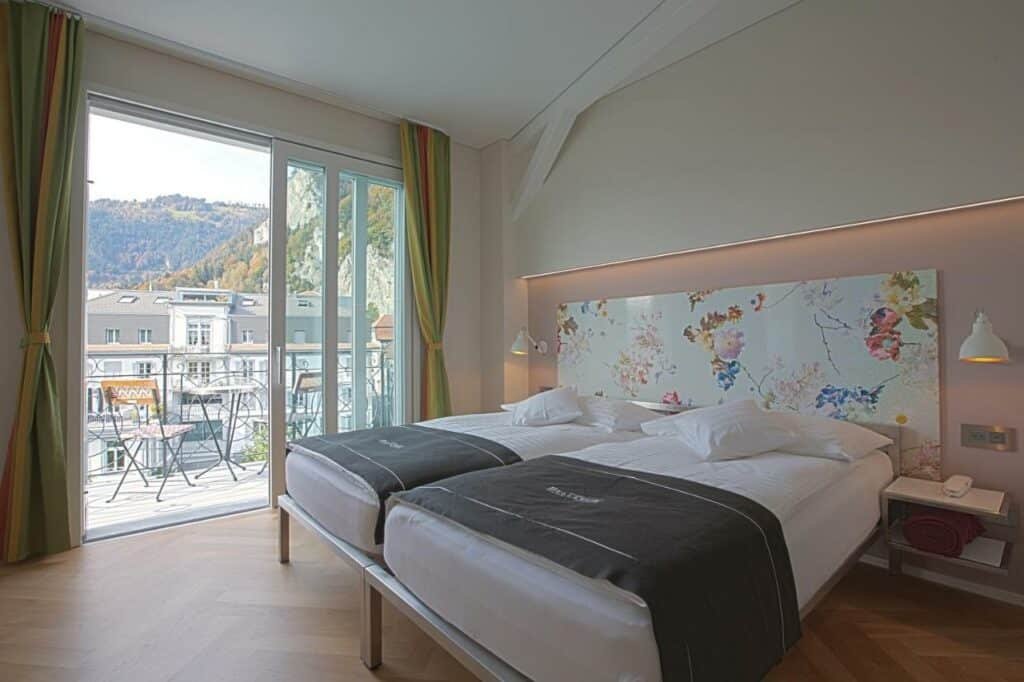 Quarto do Boutique Hotel Bellevue com cama de casal do lado direito da imagem e do lado direito um porta de vidro com acesso a varanda.
