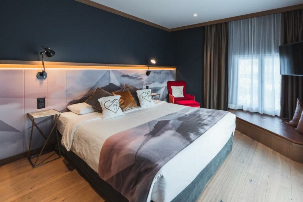 Quarto do Boutique Hotel Glacier com cama de casal do lado esquerdo da imagem, do lado esquerdo da cama uma poltrona. Representa hotéis em Lauterbrunnen.