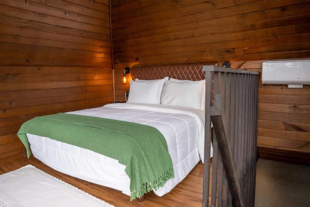 Quarto do Cabanas Cold Mountain, com cama de casal branca, luminária de ambos os lados e paredes de madeira, há ainda um ar-condicionado.