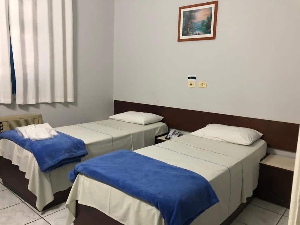 Quarto do Caiçara Hotel com duas camas de solteiro e uma janela com cortinas