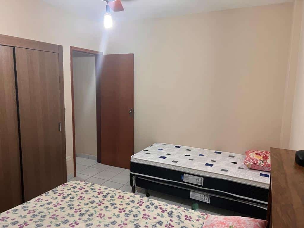 Quarto com cama de casal no lado esquerdo, cama de solteiro no lado direito, porta e armário de madeira na frente das camas. Imagem para ilustrar o post pousadas em Mongaguá.