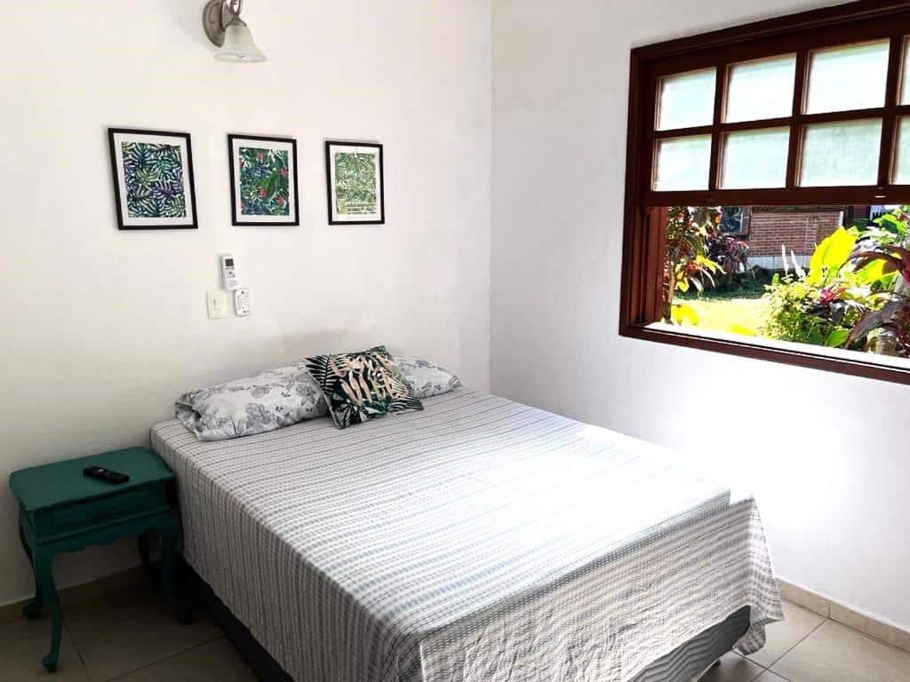 Quarto do Chales da Lua Juquehy com cama de casal do lado esquerdo da imagem no centro do quarto e do lado direito da cama uma cômoda. Representa airbnb na praia do Engenho.