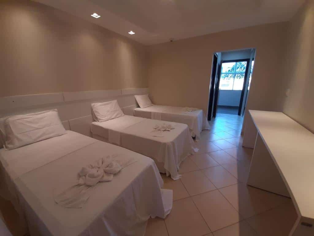 Quarto da Colônia de Férias Sindi Fast. No lado esquerdo três camas de solteiro. No lado direito uma estante de apoio de malas em toda a parede e no fundo a porta do quarto.