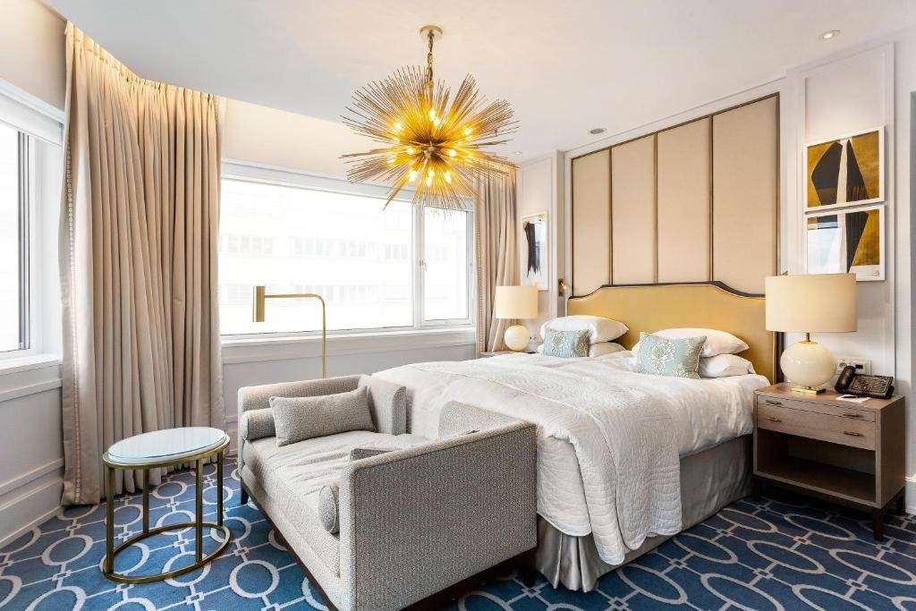 Quarto do Hotel Continental com cama ampla de casal, duas cômodas ao lado cama com luminária, janelas amplas do lado direito e sofá em frente a cama.
