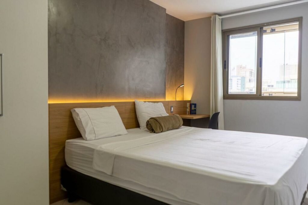 Quarto no Diamond Beach com uma cama de casal, uma janela, uma pequena mesa com uma cadeira, para representar pousadas em Vila Velha