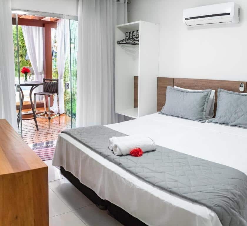 Quarto em Escarpas Eco Village, uma cama de casal, um ar-condicionado, uma varanda com mesa e cadeira, com toalhas e travesseiros sob a mesa, para representar pousadas em Escarpas do Lago