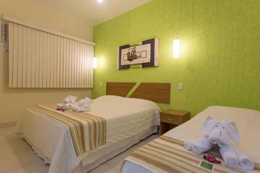 Quarto da Pousada Etoile com cama de casal do lado esquerdo perto da janela com cortinas brancas, cômoda de madeira ao meio e uma cama de solteiro do lado direito.