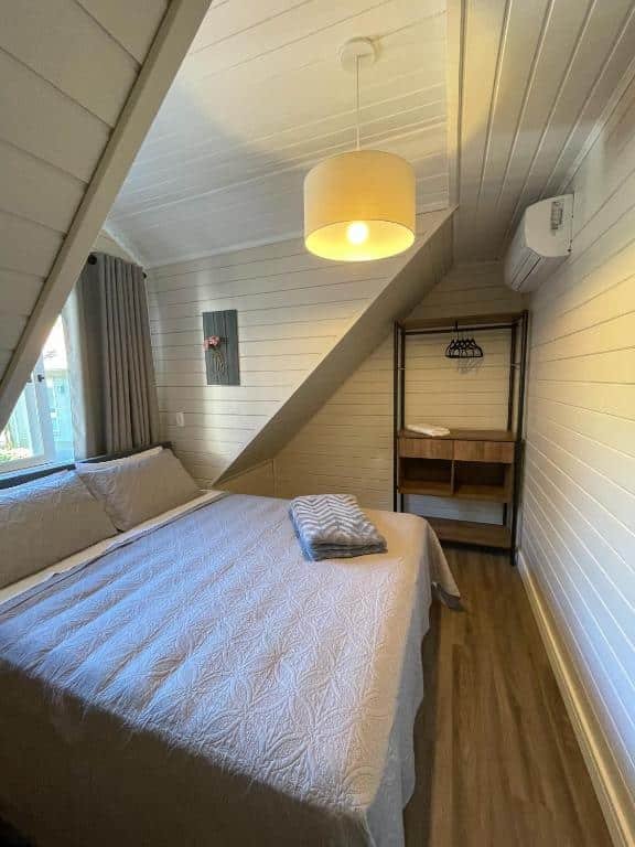 Um quarto no Family House Gramado, um armário de conceito aberto, um lustre. um ar-condicionado, uma janela e uma cama de casal, para representar airbnb em Gramado