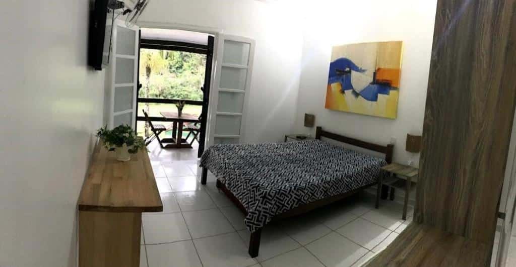 Quarto do Flat na Jureia – 30 MT da Praia com cama de casal do lado direito da imagem no centro do quarto com uma cômoda em cada lado da cama em frente a cama uma cômoda e preso na parede a TV. Representa airbnb na praia do Engenho.