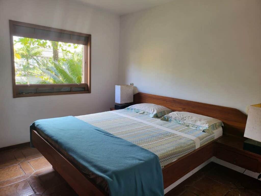 Quarto do Green Toque-Toque com cama de casal no centro e em cada lado da cama uma cômoda com luminária. Representa airbnb na praia de Santiago.