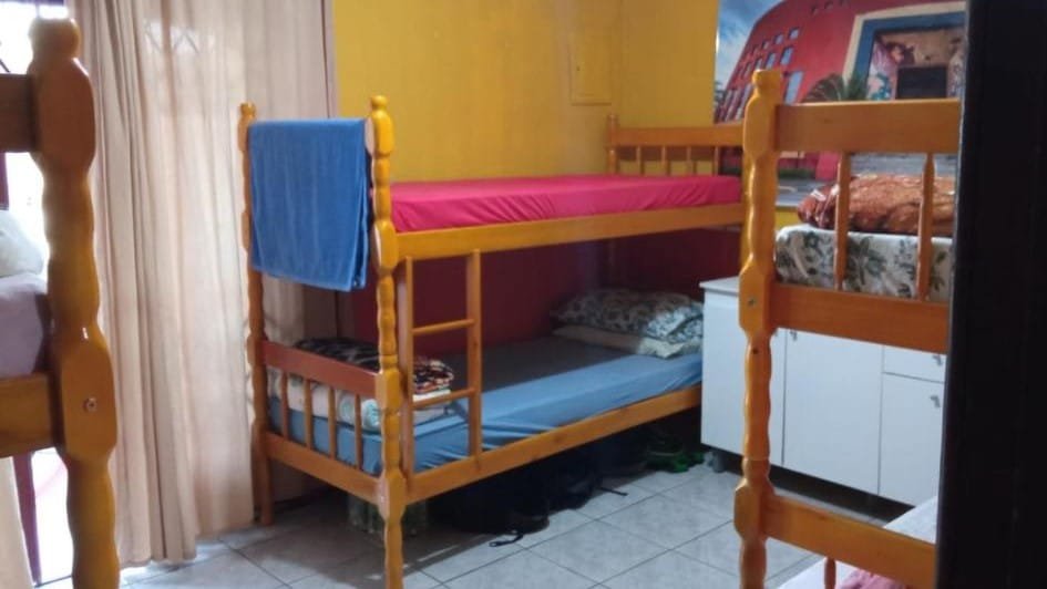 quarto do Hostel e Pousada Boa Vista em Joinville mostrando uma beliche, além de outras duas beliches parcialmente aparecendo em cada lado da imagem. Também é possível enxergar uma cômoda branca entre as beliches.