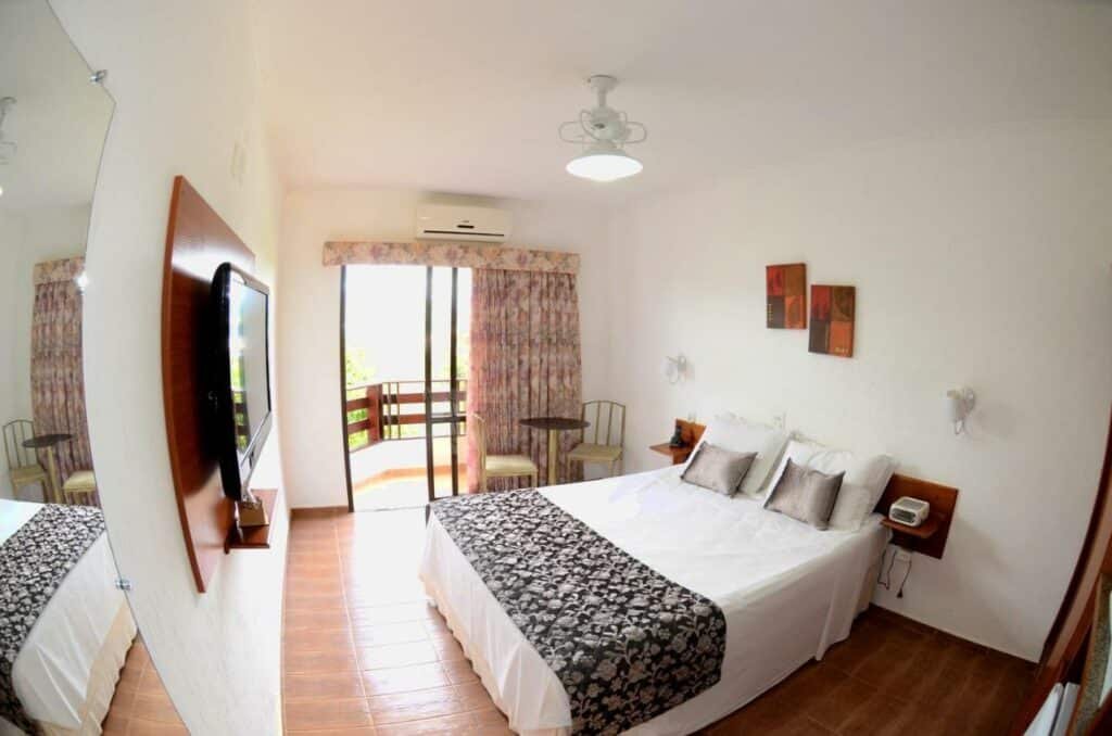 Quarto do Hotel Akropolis com uma cama de casal, uma varanda com cortinas, um ar-condicionado e uma televisão