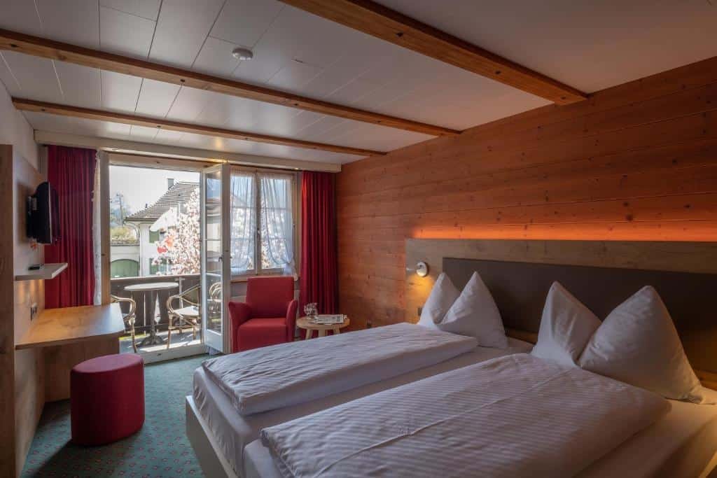 Quarto do Hotel Interlaken com cama de casal do lado direto da imagem afrente do lado esquerdo da cama uma poltrona com mesa redonda e em frente um painel com TV. Representa hotéis em Lauterbrunnen.