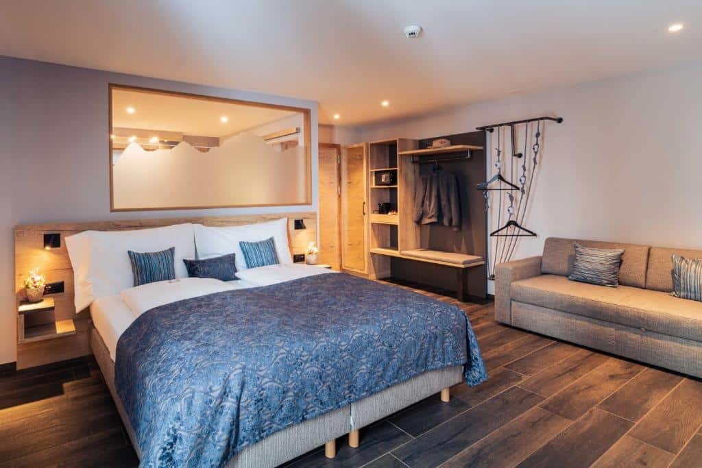Quarto do Hotel Edelweiss Superior com cama de casal do lado esquerdo da imagem do lado esquerdo da cama uma cômoda para guarda-roupa e um sofá.