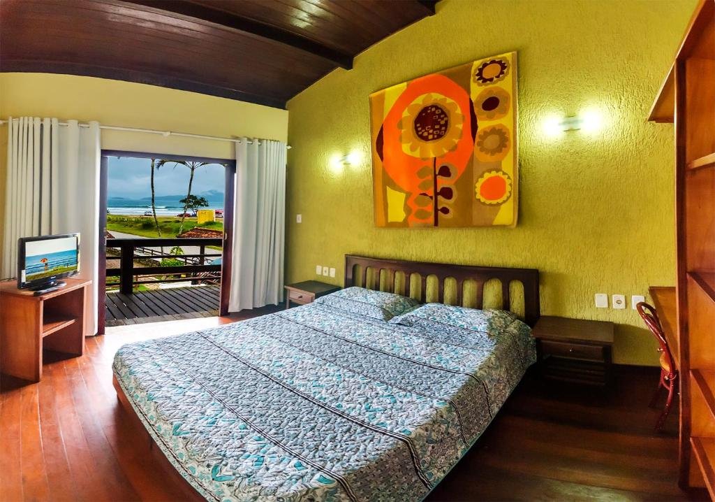 Quarto no Hotel Pousada do Sol, uma cama de casal, uma sacada, alguns armários e uma vista para a praia pela sacada, para representar pousadas na Praia do Tenório