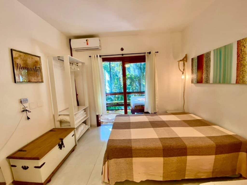 Quarto do Housing 31 – Cond. Mata Azul com cama de casal do lado direito da imagem do lado esquerdo uma cômoda e do lado esquerdo uma porta de vidro que dá acesso a varanda.