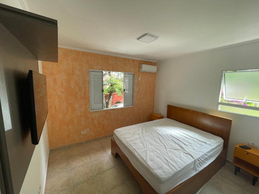 Quarto do Lar Doce Lar Toque Toque Grande com cama de casal, duas cômodas de madeiras do lado da cama e TV em frente a cama.