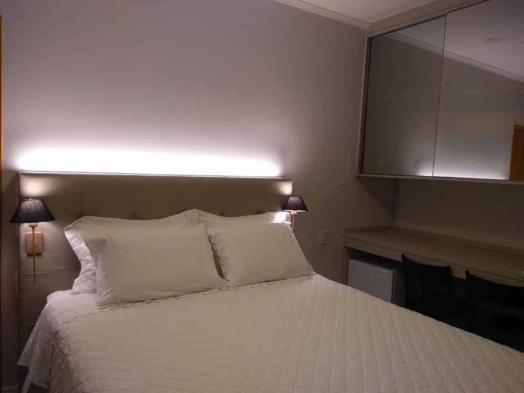 Quarto na Locanda Montecielo, uma das pousadas no Vale dos Vinhedos, com cama de casal e roupas de cama brancas, e um frigobar ao fundo