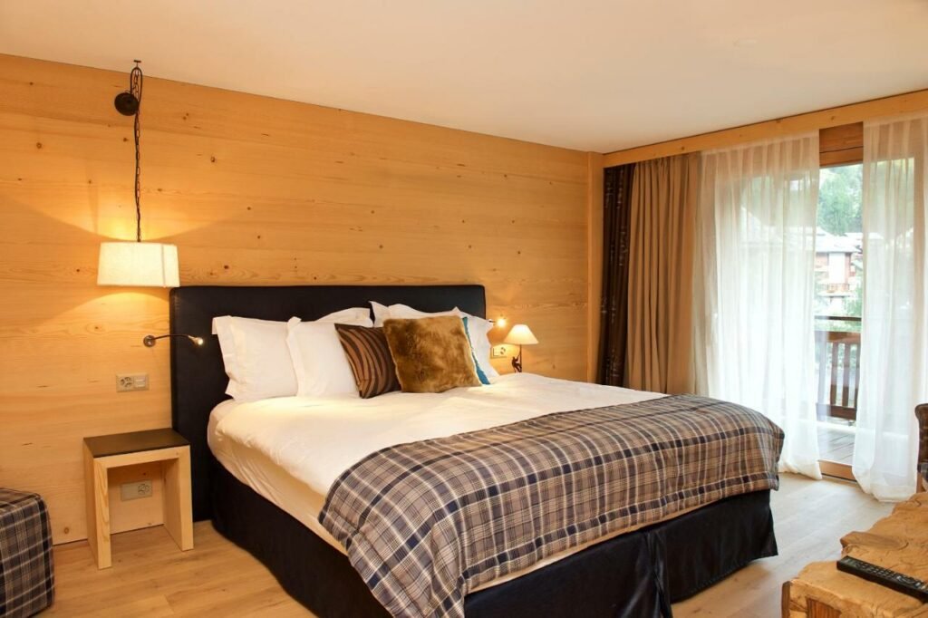 Quarto do Matterhorn Lodge Boutique Hotel & Apartments com uma cama de casal do lado esquerdo da imagem e do lado direito da cama uma cômoda. Representa onde ficar em Zermatt.