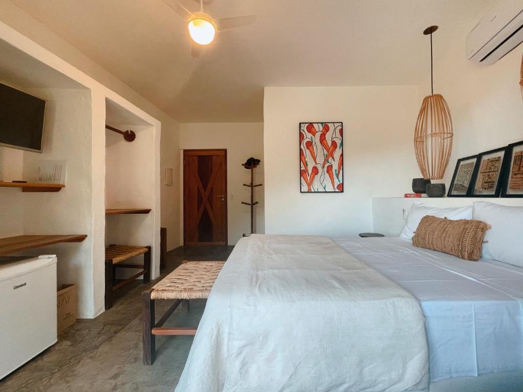 Quarto da Nai com cama de casal no centro do quarto, com frigobar a frente da cama.