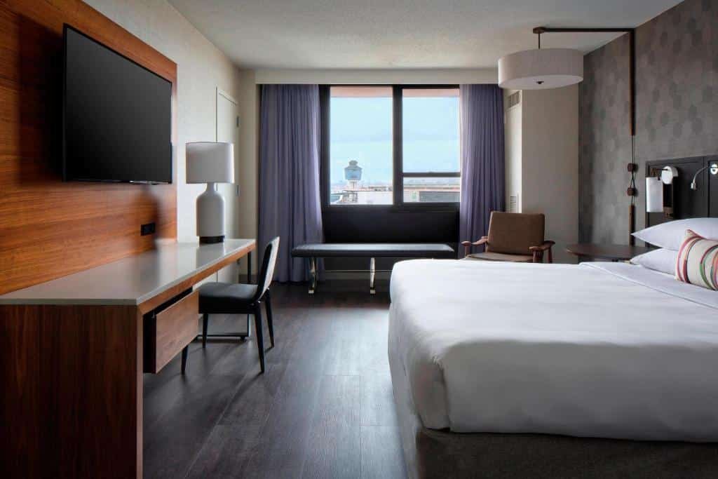 quarto do New York LaGuardia Airport Marriot com uma cama de casal à direita, uma televisão de tela plana preso à esquerda na parede, em frente a cama, e uma janela ao fundo com vista para a torre de controle do aeroporto La Guardia