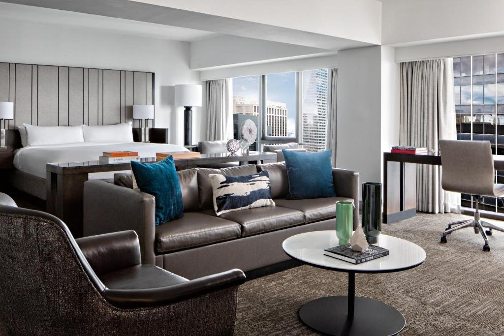 quarto do New York Marriott Marquis com uma cama de casal à esquerda, um sofá de três lugares em frente aos pés da cama e amplas janelas com vista para os prédios no lado direito da cama.