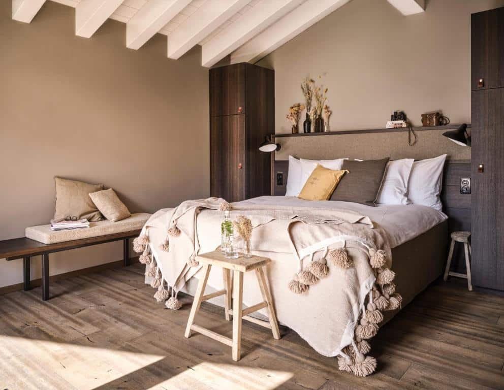 Quarto do Nomad by CERVO Mountain Resort com cama de casal do lado direito da imagem do lado direito da cama um banco estofado. Representa onde ficar em Zermatt.