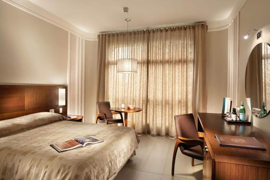 Quarto do Parque Balneário Santos by Atlantica Hotels com uma cama de casal, uma sacada com cortinas, uma mesa de escritório com uma cadeira, além de outra mesinha redonda com cadeira perto da sacada