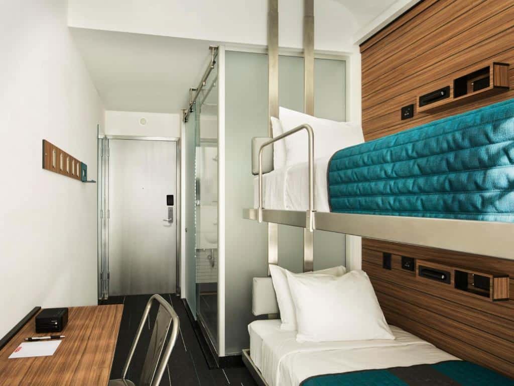 quarto do hotel Pod Times Square com uma beliche de solteiro no lado direito, uma mesa para trabalho no lado esquerdo e um banheiro ao fundo.