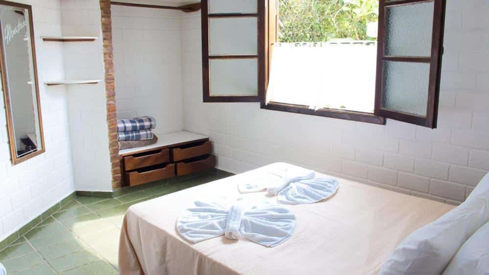 Quarto da Pousada Albatroz, uma cama de casal, um espelho, quatro gavetas, uma janela e tudo de alvenaria