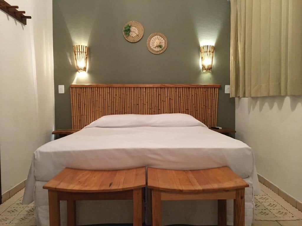 Quarto da Pousada Aroeira com cama de casal, duas cômodas de madeira ao lado da cama e duas cadeira ao pé da cama.