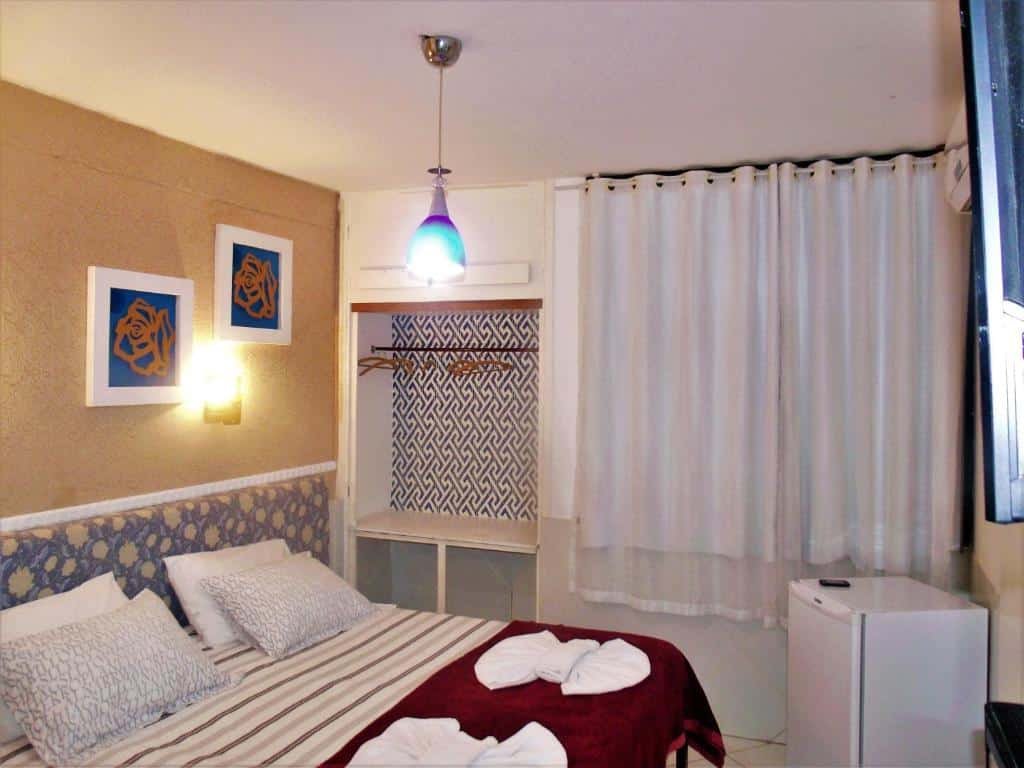 Quarto na Pousada Convento Da Penha com uma cama de casal, um frigobar, uma jenal, um armário de conceito aberto, e alguns quadros na parede