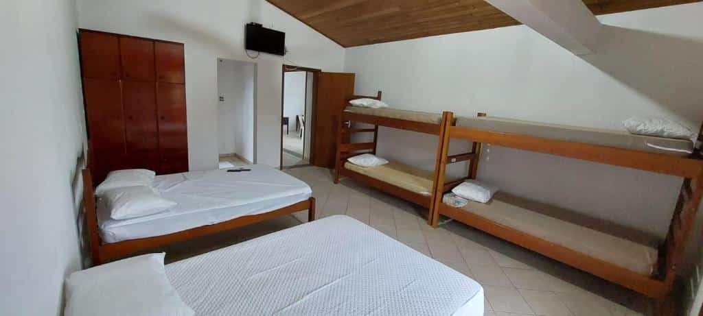 Quarto da Pousada Familiar Morada do Rapha. Duas camas de casais no lado esquerdo e atrás um guarda-roupa. Duas beliches do lado direito. Atrás, entre as camas a porta do banheiro e a porta do quarto, com uma televisão.