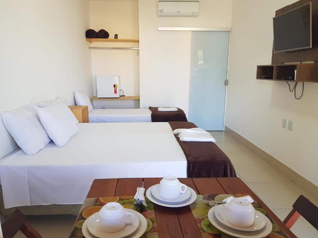 Quarto na Pousada Paraíso Mineiro, uma cama de casal, uma de solteiro, uma televisão, uma armário de conceito aberto, um frigobar, uma mesa com três lugares, para representar pousadas em Escarpas do Lago