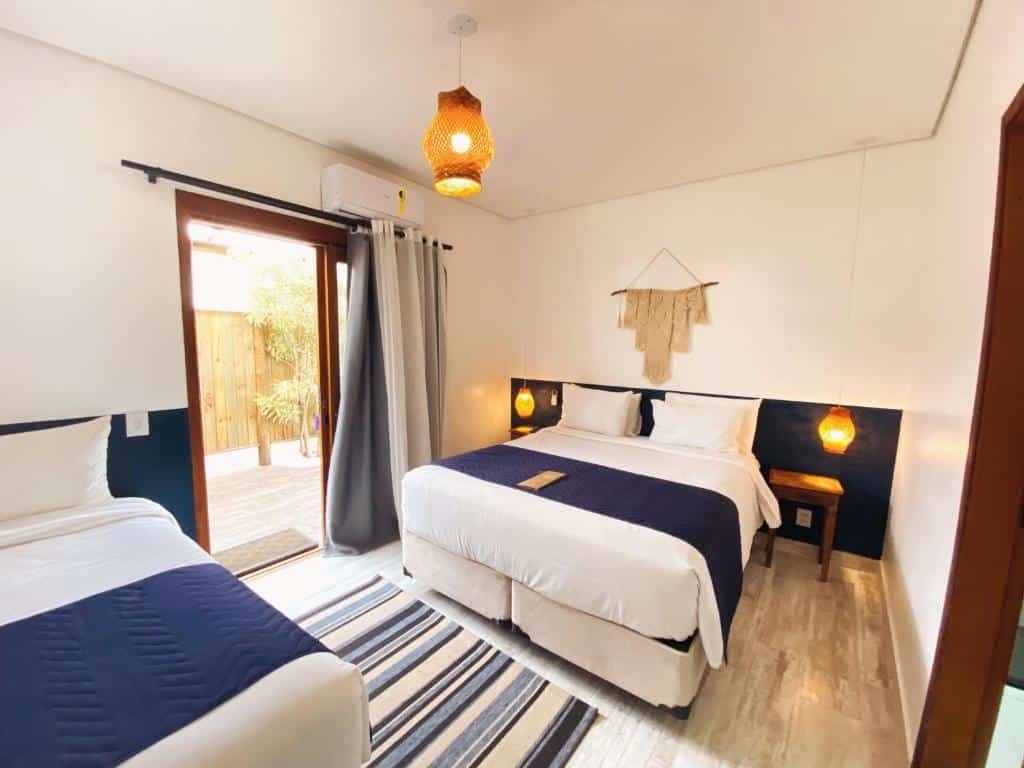 Quarto da Pousada Pono Village com cama de casal, com duas cômodas de madeira, do lado direito uma cama de solteiro perto da porta que dá acesso a varanda.
