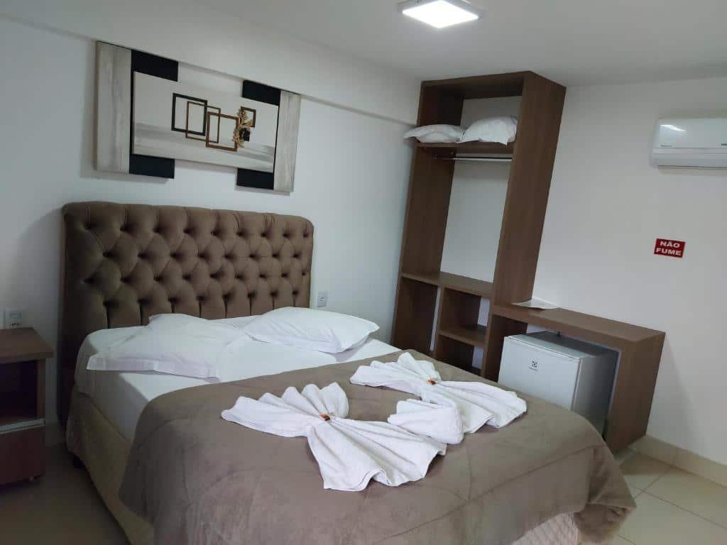 Quarto na Pousada Rainha Dos Lagos, uma cama de casal, um armário de conceito aberto, um ar-condicionado, um quadro, um frigobar, algumas toalhas e travesseiros sob a cama, para representar pousadas em Escarpas do Lago