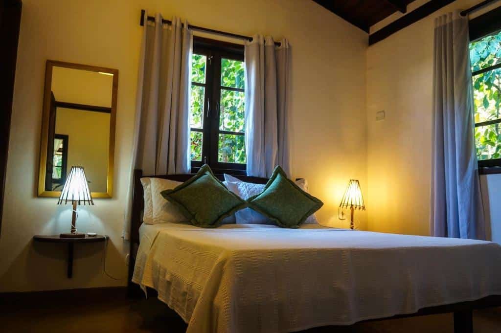 Quarto do Pousada Samambaia com cama de casal, duas luminárias ao lado da cama e um espelho do lado direito preso na parede.