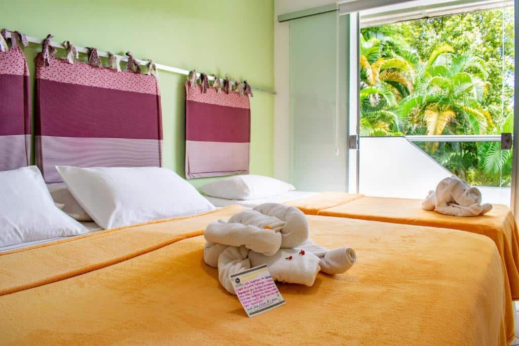 Quarto na Pousada do Tenório, uma cama de casal e uma de solteiro, uma sacada ampla com vista para o jardim, para representar pousadas na Praia do Tenório