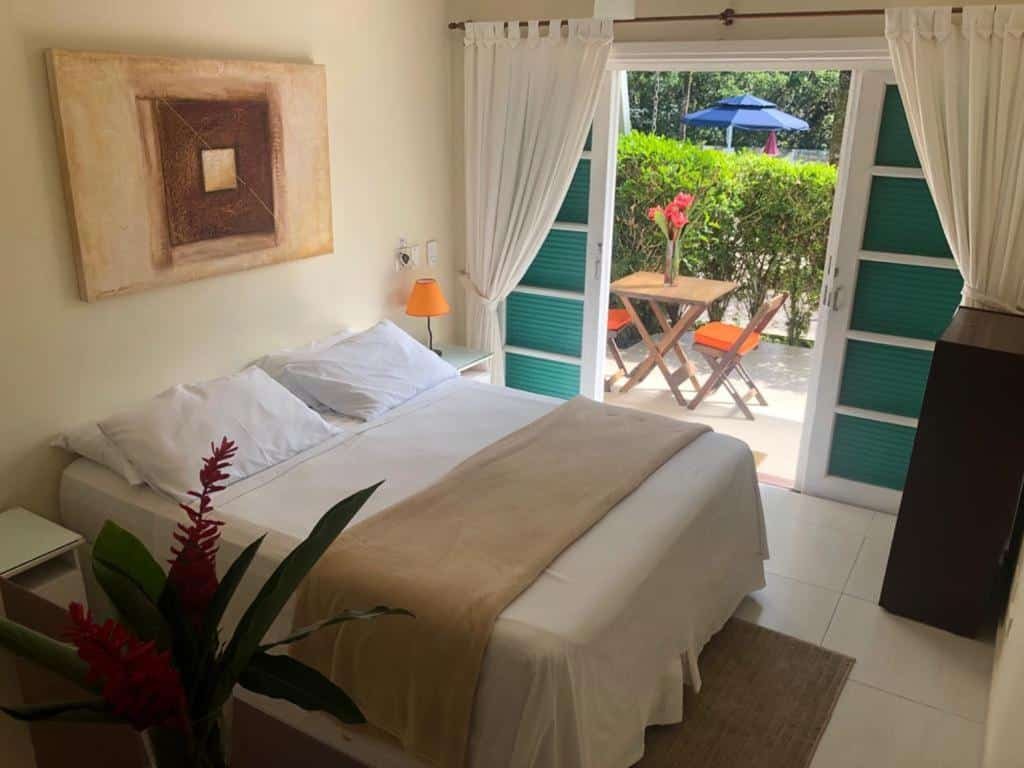 Quarto da Pousada Una com cama de casal, duas cômodas ao lado e do lado esquerdo com portas de vidro com cortinas brancas que dá acesso a varanda.