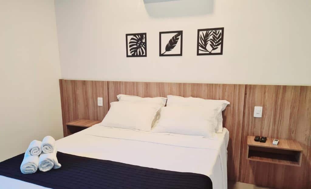 Quarto da Pousada Vila Ipuan com cama de casal ao centro, duas cômodas ao lado cama e quatro toalhas em cima da cama.