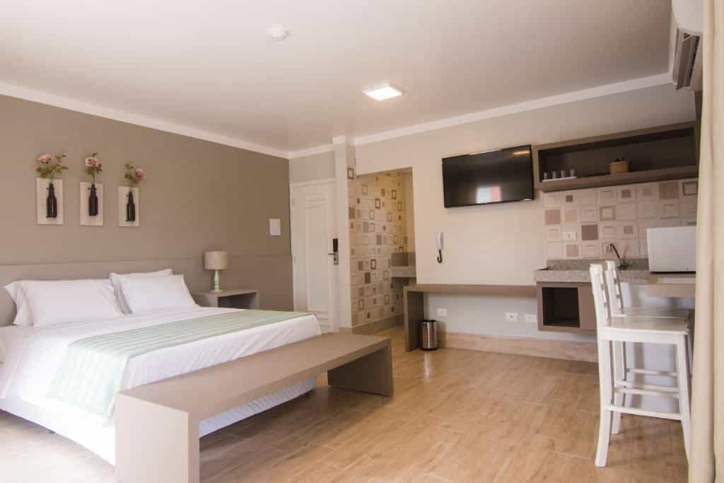 Quarto em Pousada Villa Di Enzo, uma cama de casal, local amplo, uma mini cozinha, televisão, bancada com cadeiras para se sentar, além da sacada, para presentar pousadas na Praia do Tenório