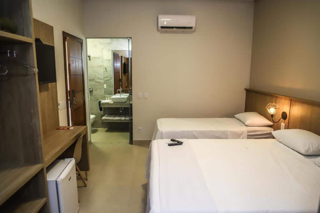 Quarto na Pousada Viver Capitólio, uma cama de casal e uma de solteiro, um abajur, um armário de conceito aberto, uma televisão e um frigobar, para representar pousadas em Escarpas do Lago